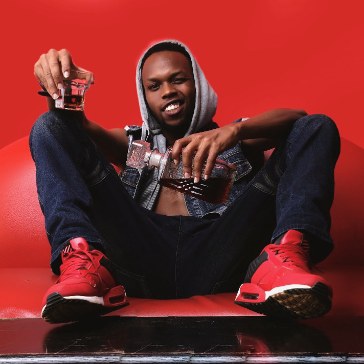 Delboy seated on a red sofa in a denim outfit and red sneakers